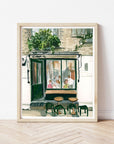 London cafe print of painting by Medjool Studio. Print of original gouache painting of a coffee shop in London, England full of customers and two small tables with stools out front.