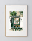 London cafe print of painting by Medjool Studio. Print of original gouache painting of a coffee shop in London, England full of customers and two small tables with stools out front.
